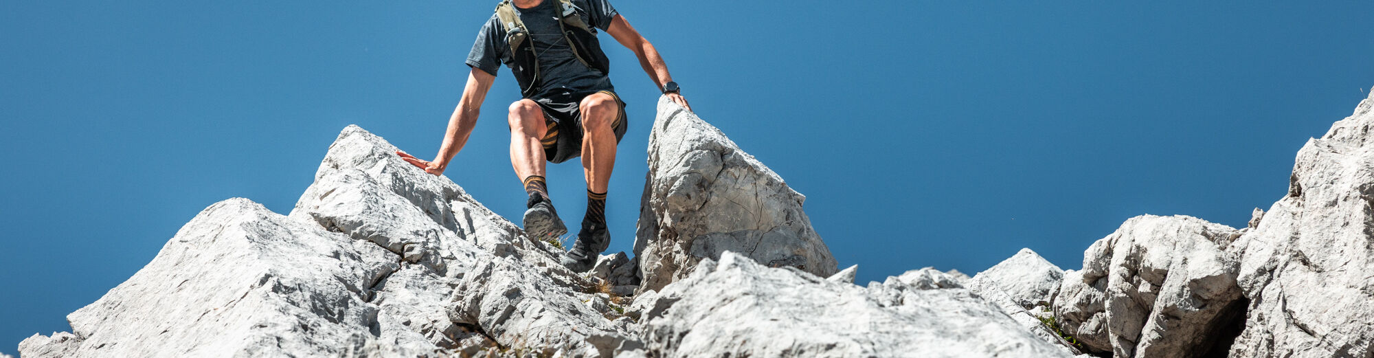 Ein Trailrunner läuft bergab und stützt sich mit den Händen im felsigen Gelände ab